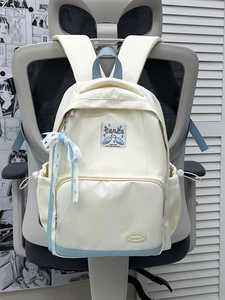 Detail view of the cream canvas backpack featuring blue accents and a light blue ribbon bow