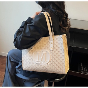 Macro detail of the beige tote bag with M letter prints and round embossed logo emblem