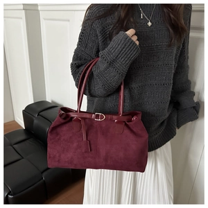 Detail of burgundy faux suede tote bag with gold buckle strap and charm accessory