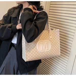 Detail view of large beige tote bag with M-pattern print and embossed logo on shoulder