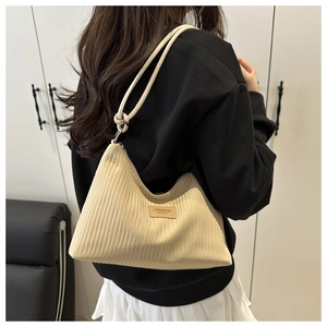 Détail d'un sac sous le bras en tissu plissé blanc cassé avec étiquette en cuir et nœud