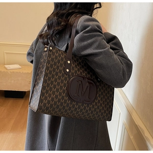 Detail showing high-capacity brown tote bag with classic M-letter monogram pattern