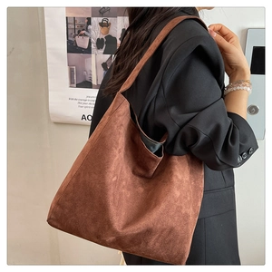 Brown suede tote bag shown on shoulder with wide strap and hobo style texture