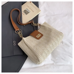 Close-up of woven straw tote bag with brown leather flap and golden chain strap detail