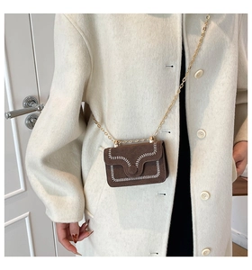 Detalle de bolso bandolera de ante café con cadena dorada sobre un abrigo de invierno
