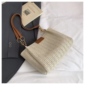 Detail of beige woven tote bag with brown leather strap and gold chain on white fabric