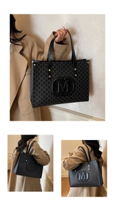 Detail of black monogram tote bag with large M logo and golden rivet strap accents