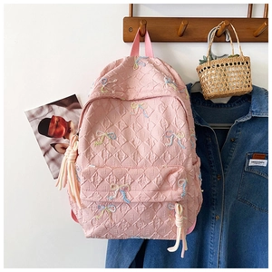Detailed close-up of light pink quilted backpack with colorful bow embroidery and rope knots