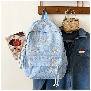 Detail of light blue quilted backpack with colorful butterfly embroidery and white tassels