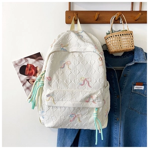 Close-up of quilted cream backpack with colorful butterfly embroidery and decorative tassel