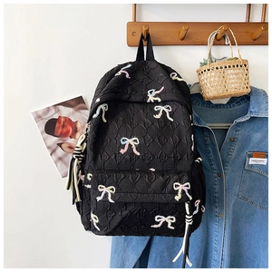 Detail of black quilted backpack with colorful embroidered bows and striped tassels