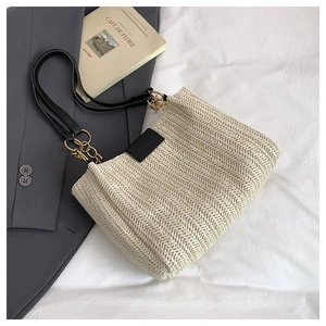 Close-up of woven straw tote bag featuring black leather straps and gold chain link detail