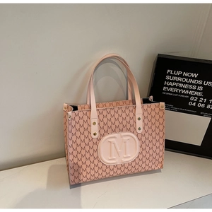 Detail of pink tote bag showing M-letter print pattern and embossed logo patch