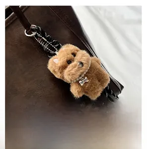 Close-up of caramel plush dog keychain with pearl necklace and metal tag on tote bag