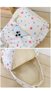 Detailed view of the front zipper pocket on a white star print backpack with a smartphone