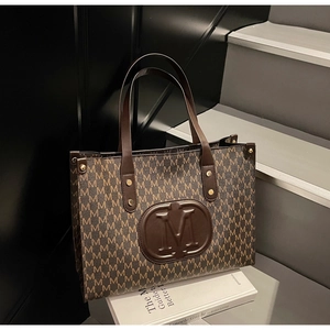 Detailed shot of brown tote bag with M letter pattern and embossed leather logo emblem