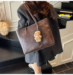 Detail view of a vintage dark brown tote bag with a cute plush bear charm on shoulder