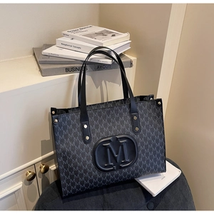 Detail of large tote bag with M-pattern print, gold studs and leather handles on a chair