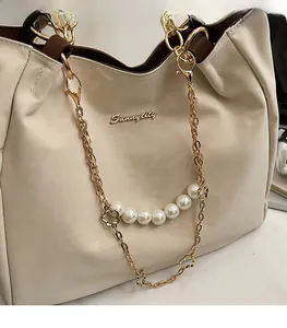 Detailed view of the elegant pearl and gold metal chain handle on this beige tote bag