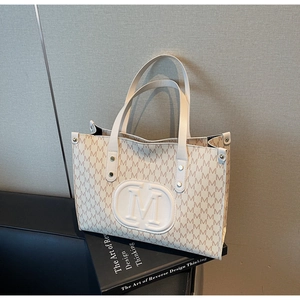 Detailed close-up of M-patterned tote bag with leather texture and rivet handle details