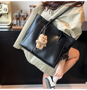 Detailed view of black patent leather tote bag with brown plush bear charm accessory