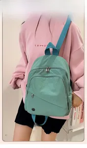 Detail view of a light green nylon backpack featuring front zip pockets and side woven label