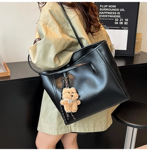 Close-up of black textured tote bag featuring a cute brown plush bear charm accessory