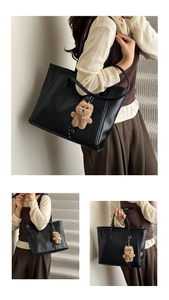 Detail view of black faux leather tote bag with brown bear charm and long shoulder strap