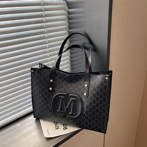 Minimalist black tote bag with M-letter print and large embossed logo on a window side