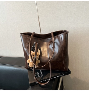 Detail of dark brown glossy tote bag with teddy bear charm on leather background