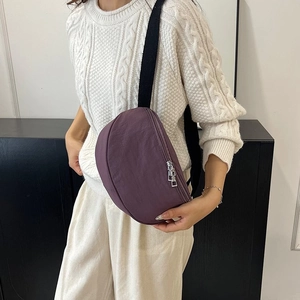 Sac banane en nylon violet en forme de croissant porté en bandoulière par un mannequin chic