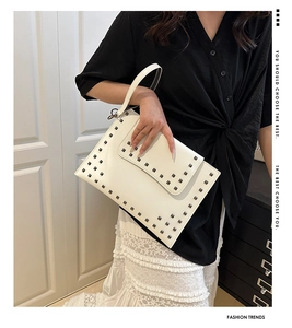 White rivet envelope clutch bag held by model wearing a black shirt and lace skirt