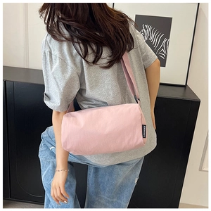Side view of a pink nylon barrel crossbody bag featuring a branded woven label on a model