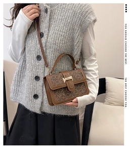 Detailed view of brown letter print handbag with vintage buckle on a model in a home setting