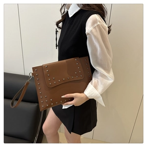 Close-up of brown textured envelope clutch featuring silver square rivets and wristlet