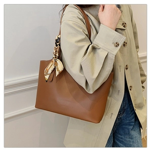 Brown leather tote bag with silk scarf detail worn by a model against a white wall