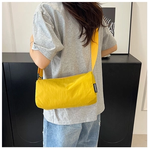Detail view of the yellow nylon crossbody bag with side logo tag and wide strap