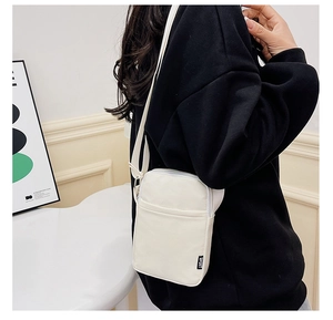 Detail view of a compact cream nylon crossbody bag featuring a Sport woven label and strap