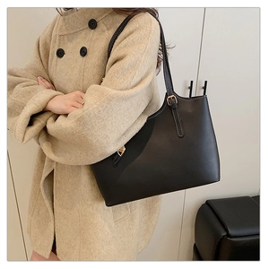 Detail view of a black leather tote bag with white stitching on a beige wool coat