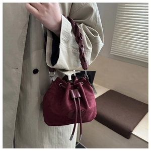 Detail view of burgundy suede bucket bag with woven handle and drawstring closure