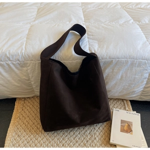 Détail d'un grand sac cabas en daim marron foncé sur un tapis tissé dans un décor douillet