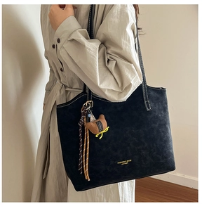 Detailed texture of black faux suede tote bag with woven cord side and plush charm