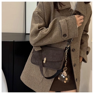 Detail of dark brown shoulder bag with gold peanut buckle and plush pendant charm