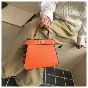 Detailansicht der orangefarbenen Ledertasche mit goldenem Drehverschluss und Einzelgriff