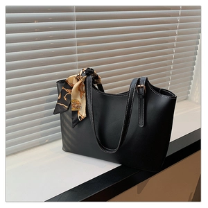 Detail of a black tote bag with white stitching and decorative silk scarf by a window