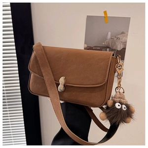 Close-up of brown matte leather crossbody bag with peanut-shaped metal buckle and plush charm