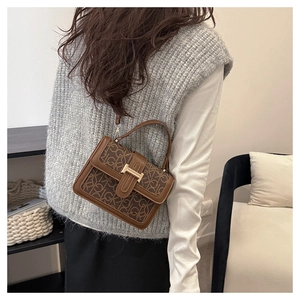 Detail of a brown monogram crossbody bag with gold H-buckle on a stylish grey sweater