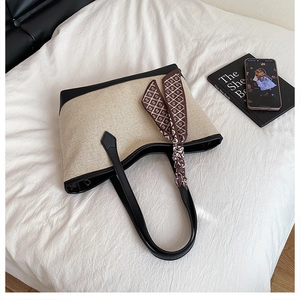 Dettaglio della borsa tote in tela beige con manici neri e foulard di seta stampato decorativo