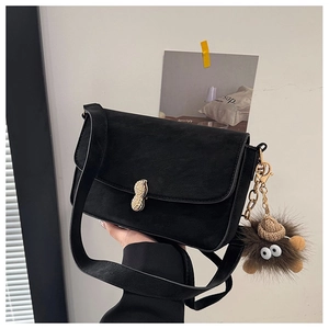 Detail of black matte crossbody bag featuring a golden peanut buckle and plush charm