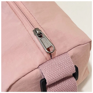 Detail of pink nylon bag with gray metal zipper and adjustable woven strap buckle